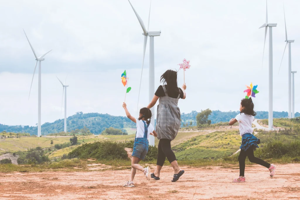 Mother and two daughters running in a field with wind turbines in the background.